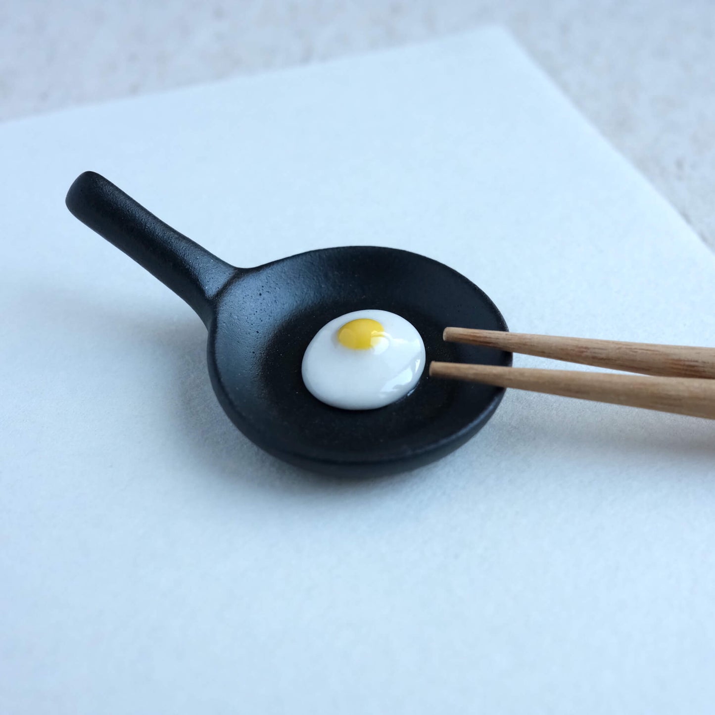 Chopsticks resting on a fry pan with egg chopstick rest.