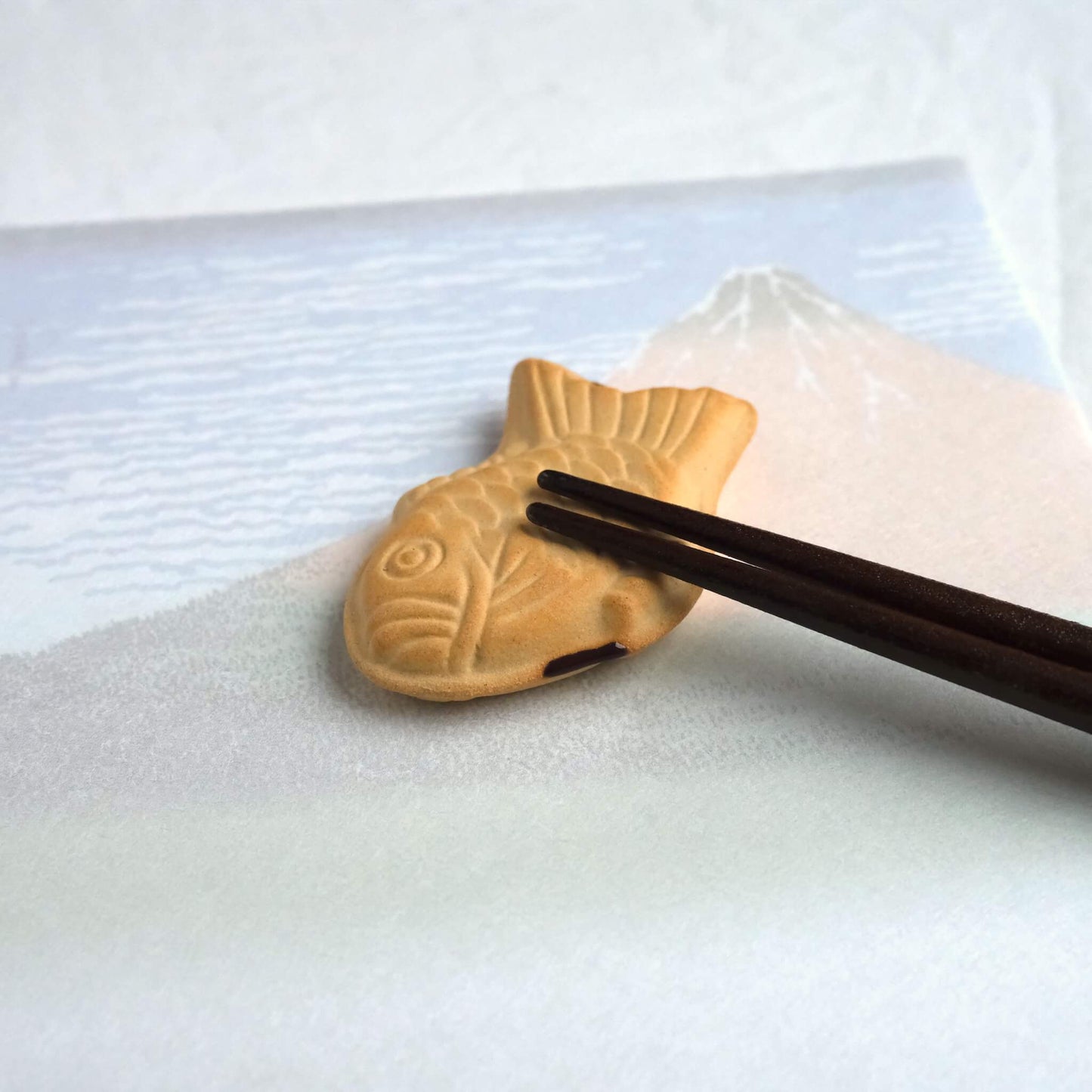 Chopsticks resting on a taiyaki chopstick rest.