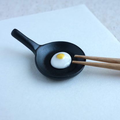 Chopsticks resting on a fry pan with egg chopstick rest.