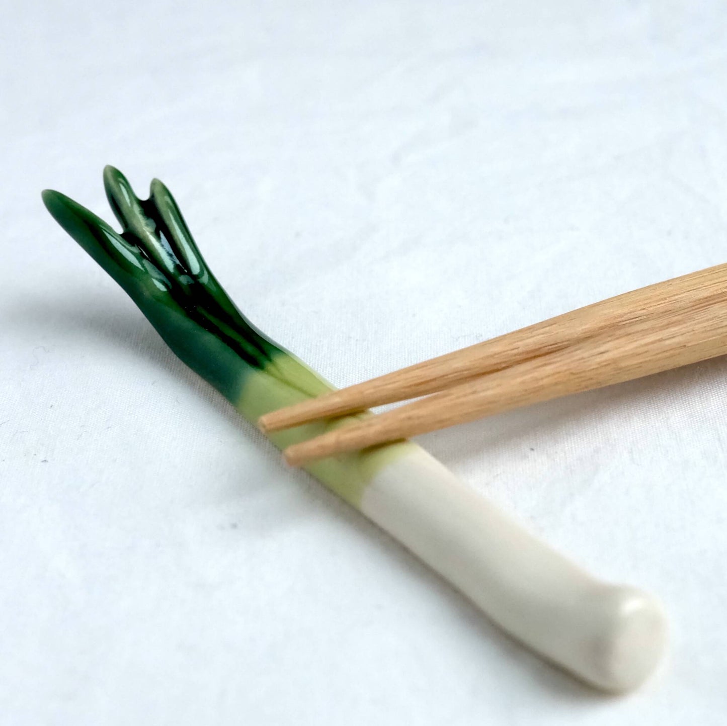 Chopsticks resting on a green onion chopstick rest.
